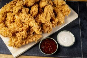 Delicious golden fried chicken tenders served with spicy and creamy dipping sauces on a platter.